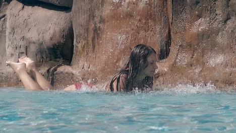 girl lies under artificial blue waterfall and swings legs