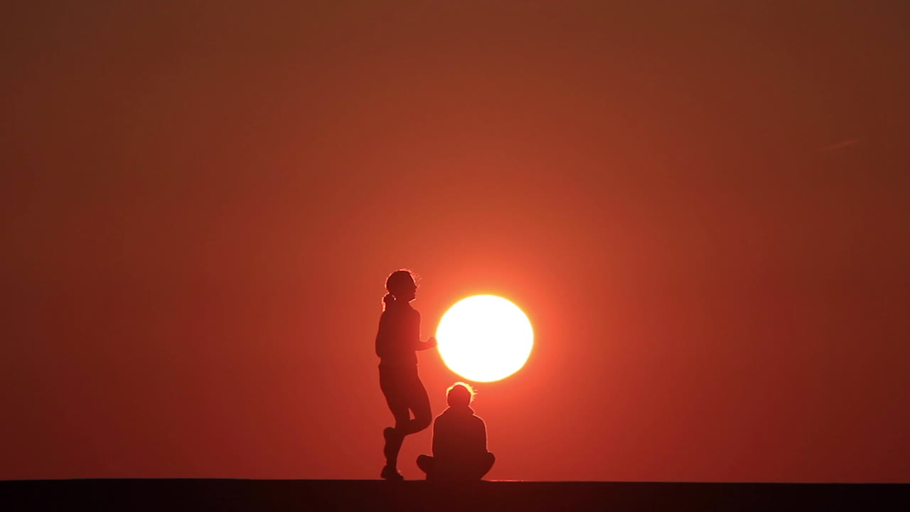 Silhouette of a man in front of the rising sun in the morning while a female runner passes by at Chicago's North Avenue Pier along Lake Michigan.