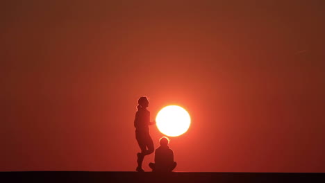 silhouette of a man in front of the rising sun in the morning while a female runner passes by at chicago's north avenue pier along lake michigan.