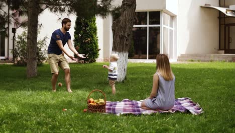 front view of an idyll family hanging out together in the park. young mom sitting on a grass and watching his son playing. father amuses son, throws cones into the air. slow motion