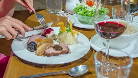 close up decorative dinner on plate with red wine at restaurant, female hand hold fork and knife, static shot