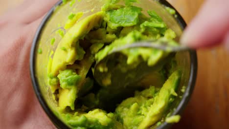 avocado pulp in a glass being mixed with a spoon