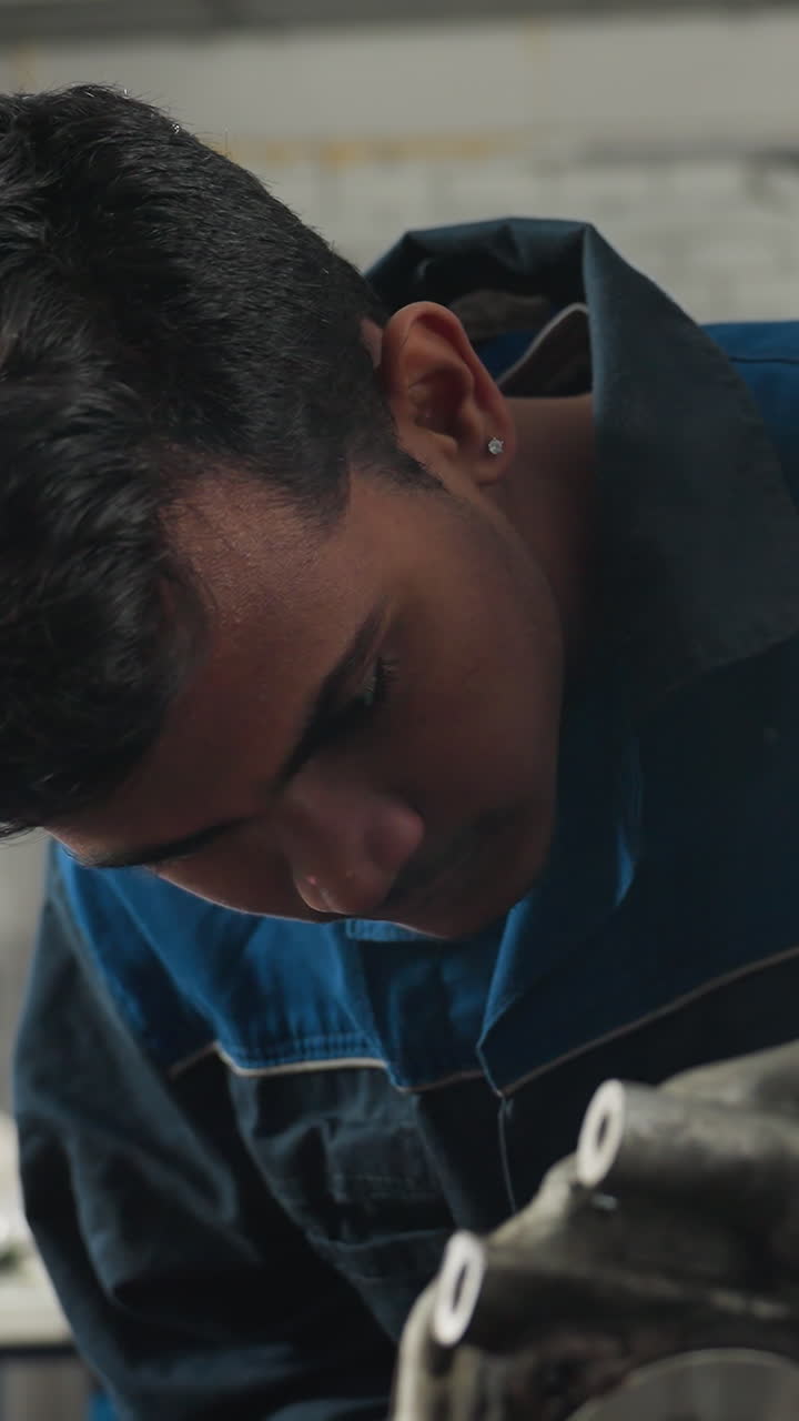 Riparatore di motori concentrato sul lavoro al motore in un'officina automobilistica, con una vista parziale di un collega che gli mostra qualcosa, circondato da attrezzi meccanici.
