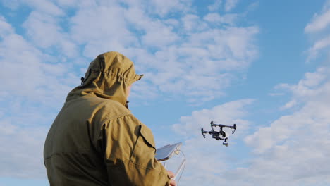 the man controls the drone which is floating in the air around him against the background of blue sk