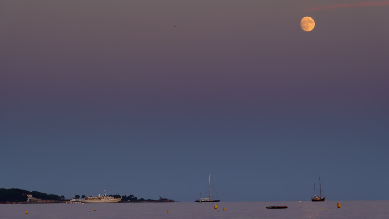 Boats on the sea in the evening with the moon up in the sky