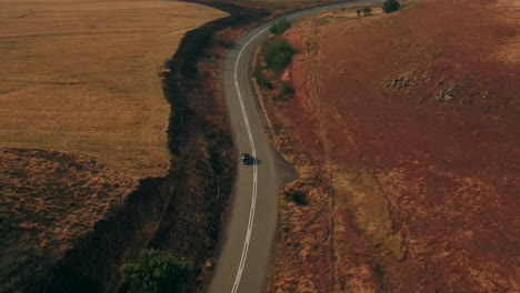 Disparo-De-Dron-Alto-Y-Ancho-Después-De-Un-Automóvil-Antiguo-Negro-Austin-Westminster-Conduciendo-A-Través-De-Las-Colinas-De-Sudáfrica-Durante-El-Invierno-Seco-4k