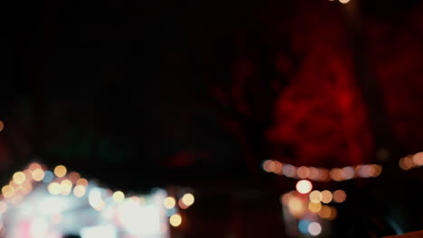 close up de una mujer con guantes de cuero negro haciendo una forma de corazón con sus manos durante una noche en un mercado de navidad con luces en el fondo en cámara lenta
