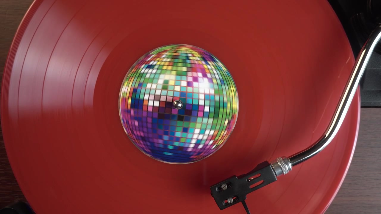 Riproduzione di un disco in vinile rosso, che gira su un giradischi con puntina e adesivo a forma di palla da discoteca, vista dall'alto