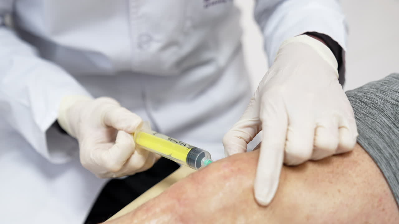 Unrecognized medic is putting a syringe into male knee. Plasmolifting therapy in hospital.