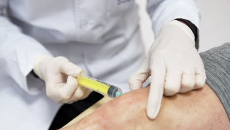 unrecognized medic is putting a syringe into male knee. plasmolifting therapy in hospital.