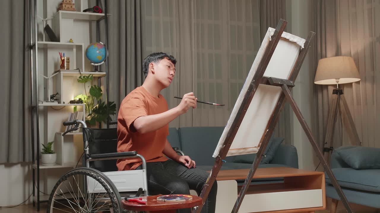 Asian Artist Boy In Wheelchair Holding Paintbrush Mixed Colour And Thinking Before Painting On The Canvas