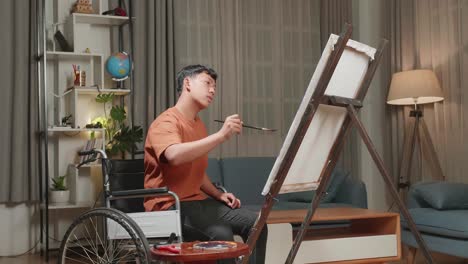 asian artist boy in wheelchair holding paintbrush mixed colour and thinking before painting on the canvas