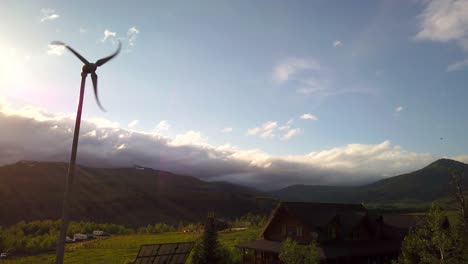 A-wind-turbine-is-seen-spinning-near-a-cabin-with-a-mountain-nearby