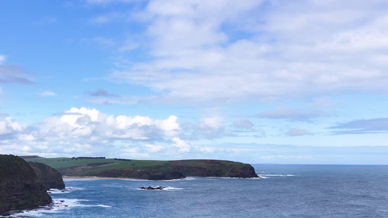Wide panoramic shot of rocky coastline, ocean waves, and cliffs under bright daylight, slow pan
