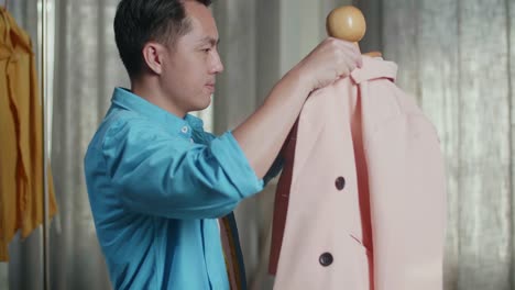 close up of asian male designer with sewing machine wearing jacket on a mannequin while designing clothes in the studio