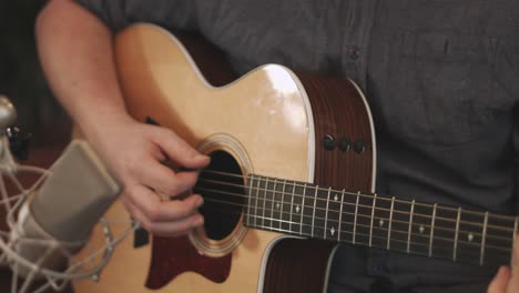 primer plano de un cuerpo de guitarras acústicas occidentales tocado por un músico profesional durante una sesión de grabación con un micrófono de condensador de diafragma grande colocado delante