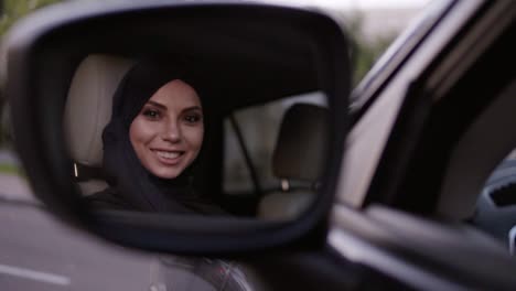 Car-Mirror-Reflection-Shot-Of-A-Happy-Young-Muslim-Woman-In-Black-Hijab-With-Professional-Makeup