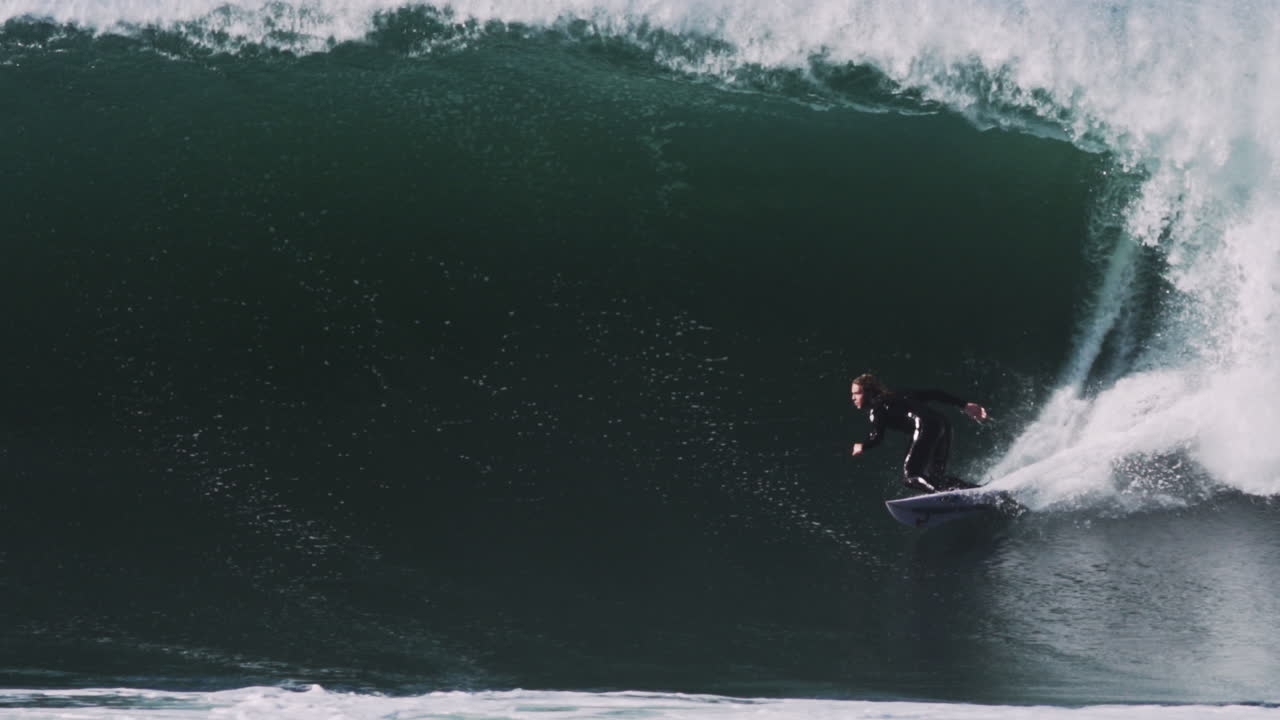 Foam and spray erupt as surfer exits fast barreling tube in explosive speed