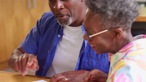senior couple sitting around table at home reviewing finances using digital tablet
