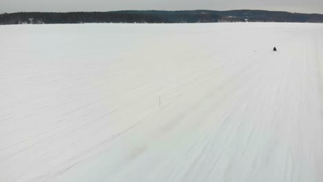 tracking aerial shot of a man driving his snowmobile on indalsalven in timra, sundsvall, sweden