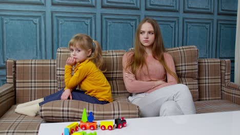 unhappy mother and stubborn little child daughter ignoring each other sitting on couch after quarrel