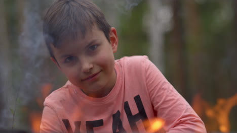 niño adolescente mirando con antipatía a través de la línea de fuego de la llama en el bosque.