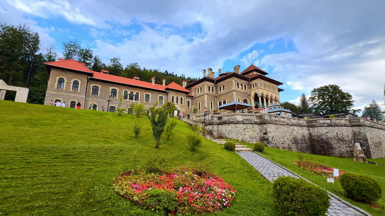 Busteni, Romania, 17 July 2025: Lovely flower bed and green mowed lawn in front of Cantacuzino Castle in Busteni, Romania. Tourists walk around the historical building
