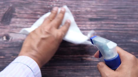 cleaning a wooden table with a spray bottle and tissue