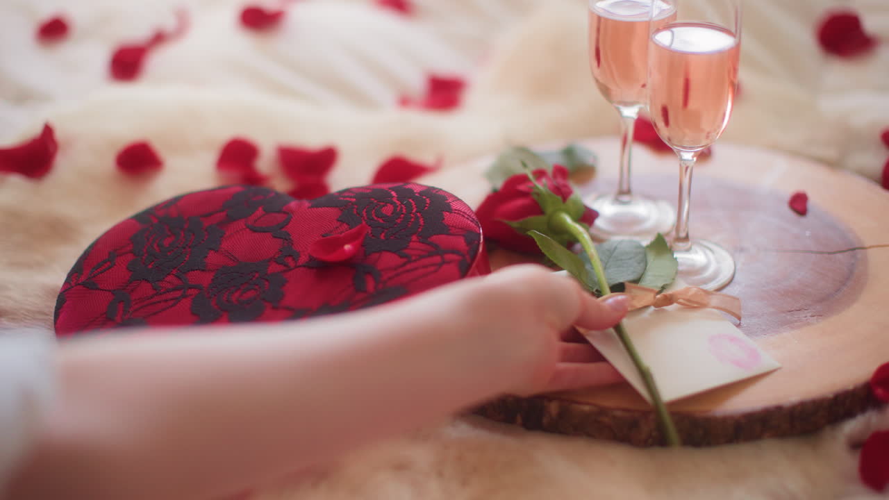 Woman's hands placing Valentine's Day card and rose on wood platter
