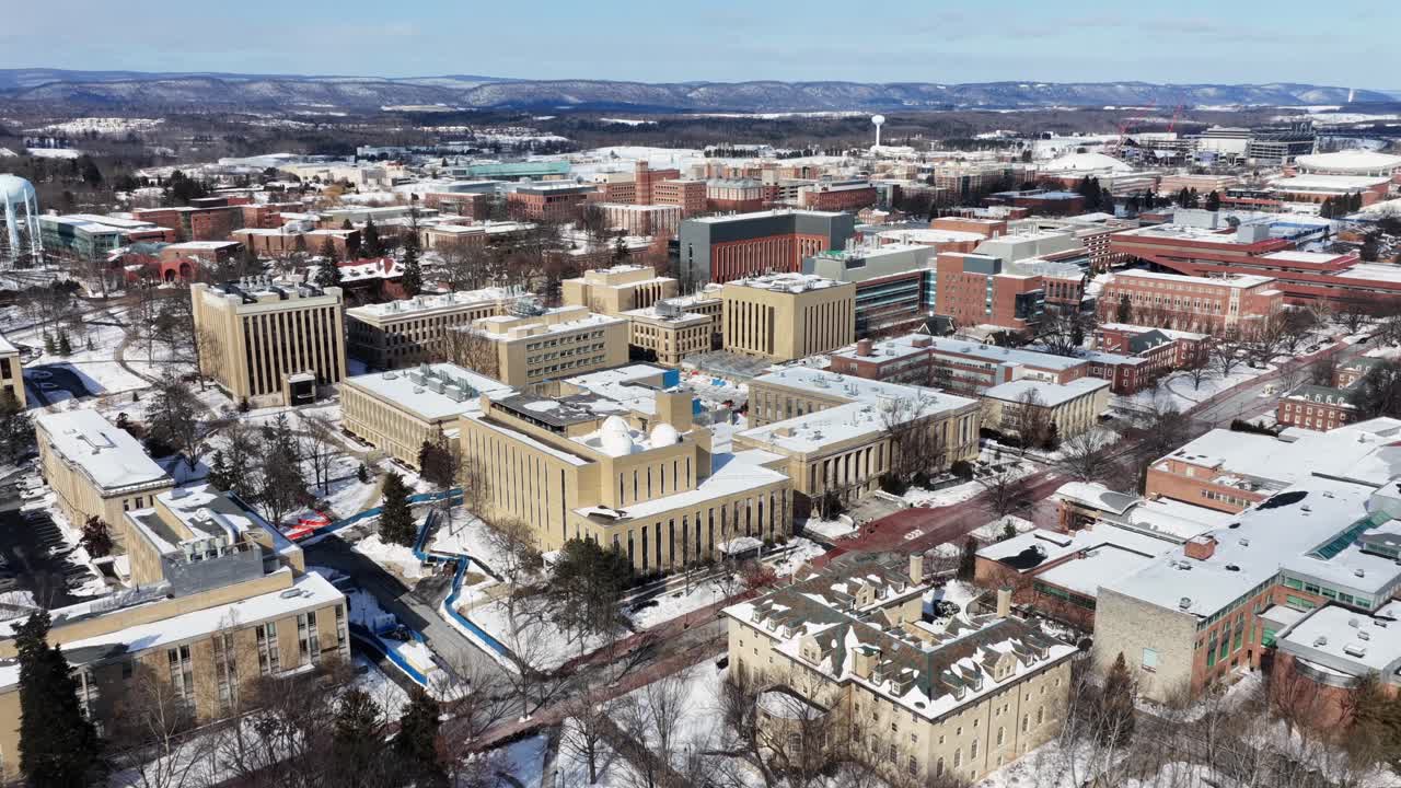 Vinterbillede fra luften af Penn State Universitys campus i State College, Pennsylvania, med akademiske bygninger og stier dækket af frisk sne under klar himmel. Panorama oversigtsbillede.