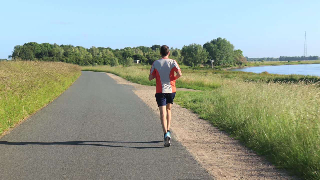 disparo en movimiento constante de un corredor de trail masculino visto desde atrás corriendo por el asfalto de las llanuras de inundación del valle del dique en el paisaje del río holandés ijssel