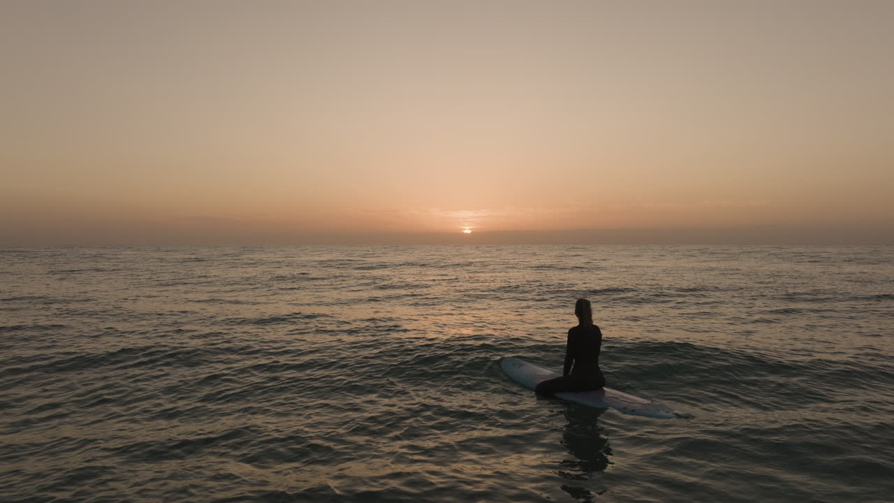 surfer girl sitting on surfboard and watch the sunrise over the Atlantic Ocean on Fuerteventura Canary Islands