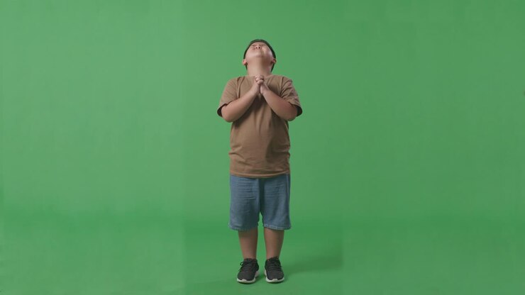 Full Body Of Asian Boy Pray For Something While Standing In The Green Screen Background Studio