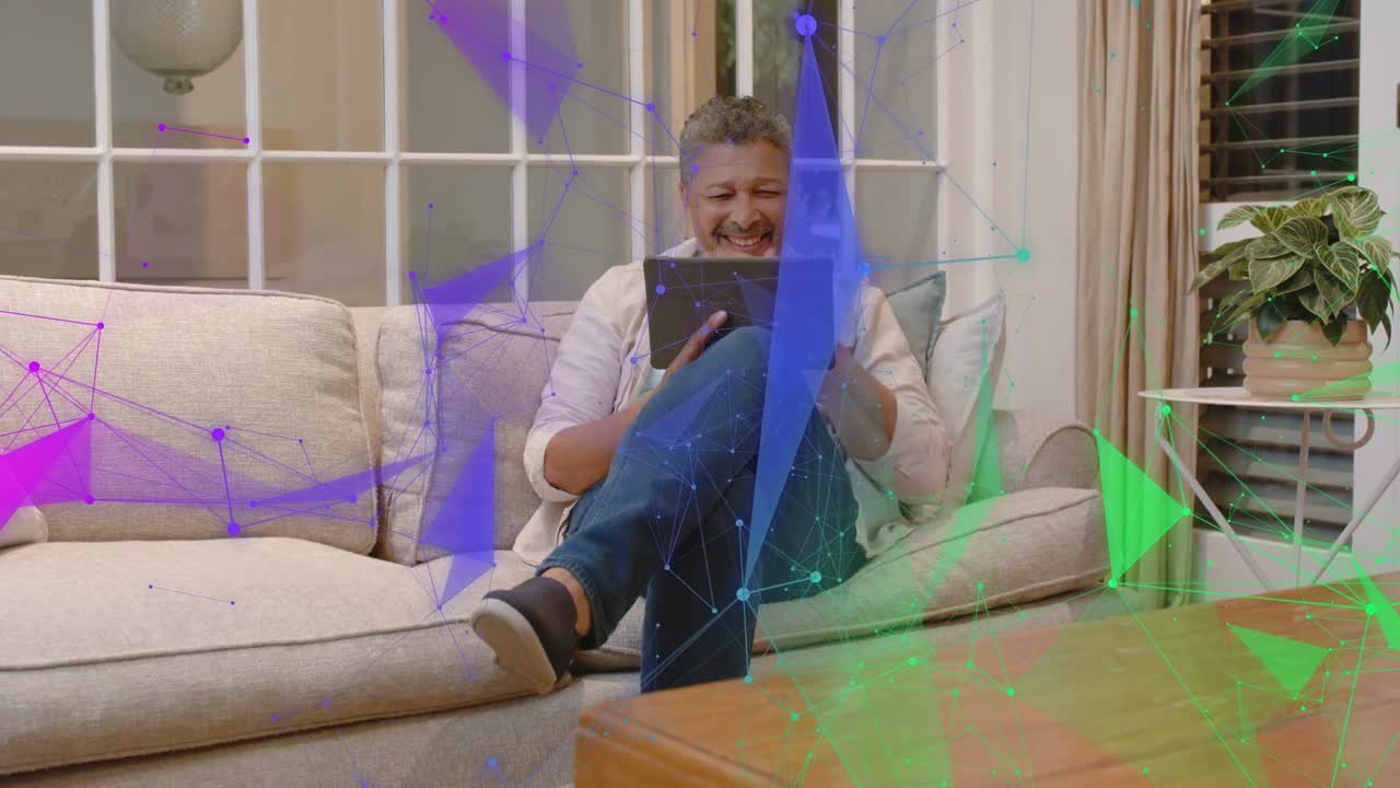Uomo maturo seduto sul divano che tocca e scorre sul tablet, avviando sovrapposizioni tecnologiche e sorridendo.