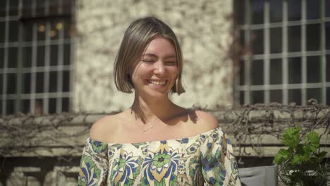 portrait of a beautiful dark haired european woman smiling charmingly while standing in front of an old wall, wearing beautiful top