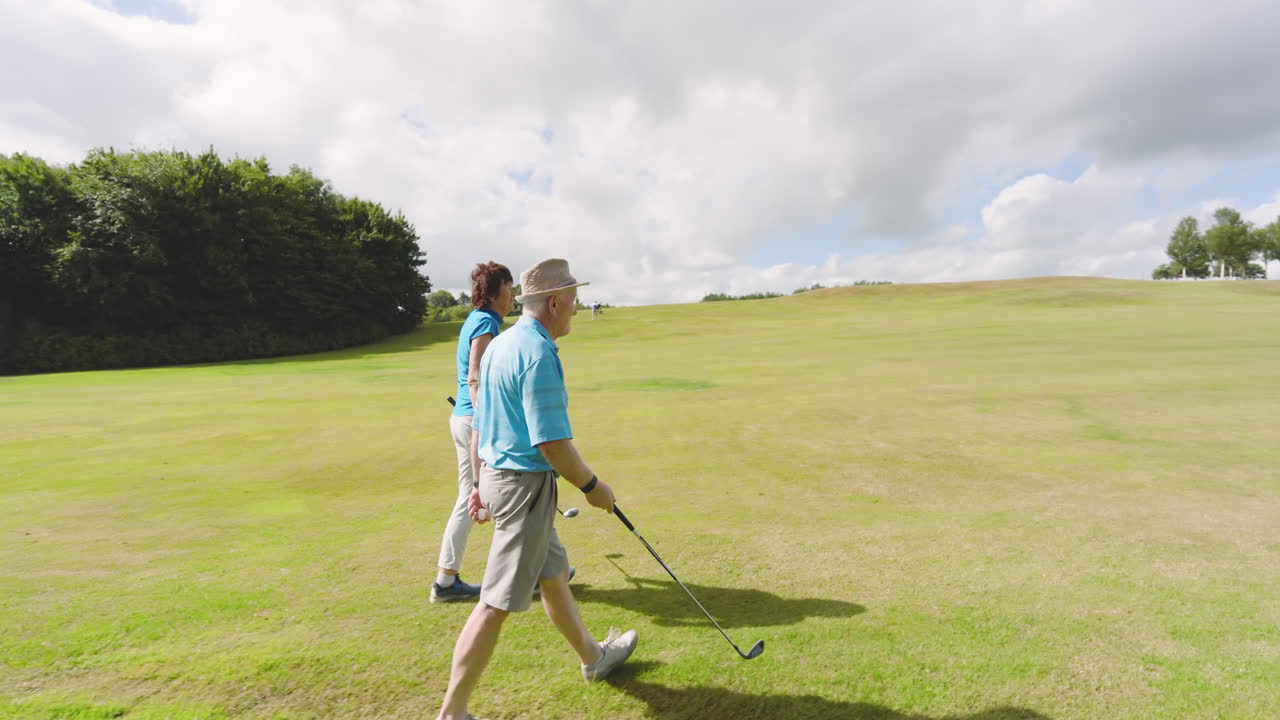 Male and female golf players wearing uniforms, talking and walking with clubs on golf course
