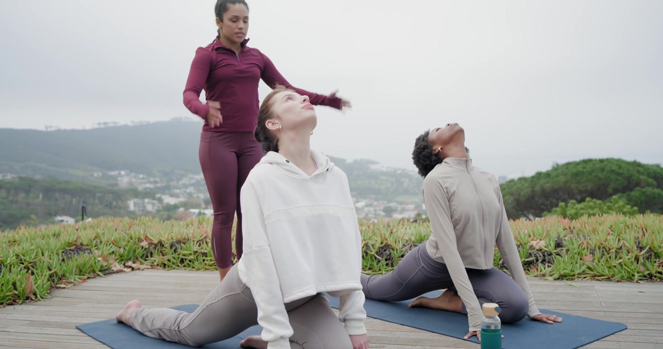 Diverse donne yogi che eseguono un inarcamento all'indietro su tappetini blu sul ponte, con l'insegnante che si avvicina per guidare la postura.