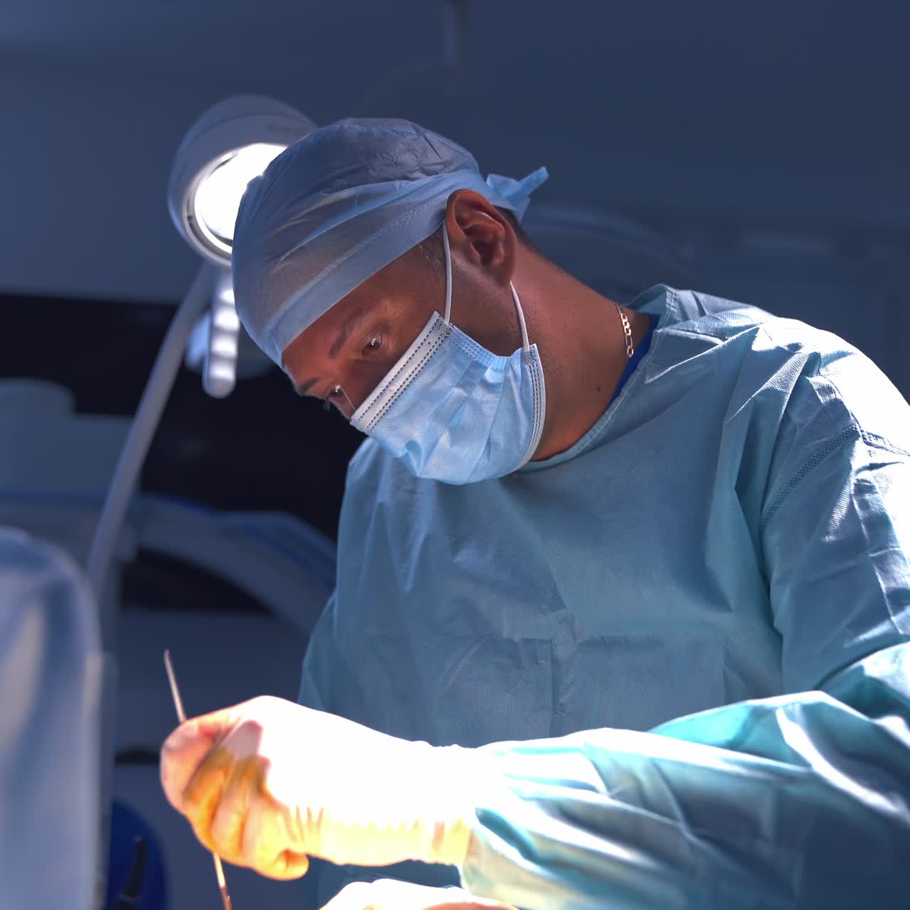 Surgeon using medical scissors during plastic surgery in the operating room. Professional plastic surgery specialist in mask