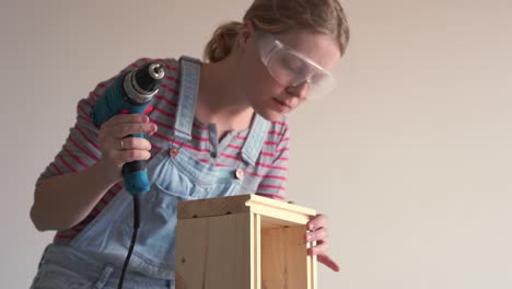 a woman does a non-female job - drills a hole with a screwdriver in a wooden box