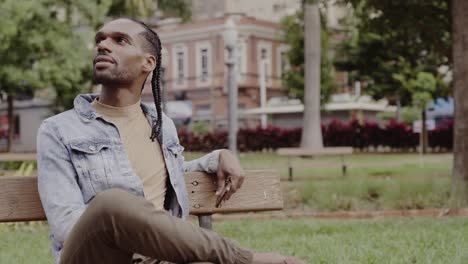 man with braids smiling and relaxing on a park bench