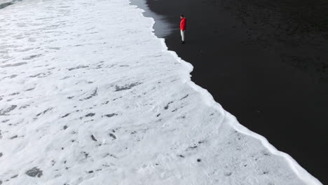 man standing at reynisfjara black sand beach with foamy waves in vik, iceland