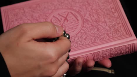 a person doing dhikr on a prayers beads while holding a quran in the other hand