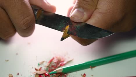 footage of hands slowly sharpening a pencil and some coloured pencils with a sharp knife