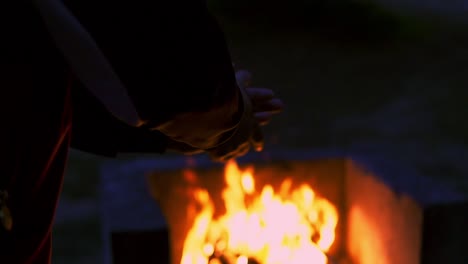 slow motion shot of a man clapping in front of a campfire at night