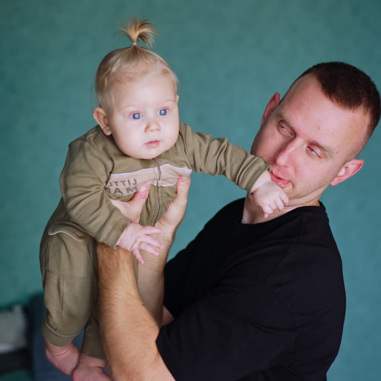 Man is holding his little child in front of him. Dad making faces to a kid and entertains the baby