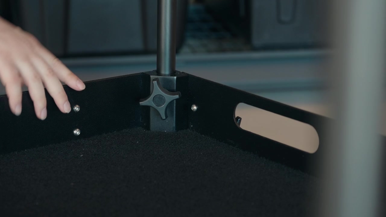 Static close-up shot of a man tightening a black adjustment knob on a camera cart mounting point before securing the support pole