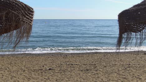 Tiro-De-Cardán-Estabilizado-En-4k-Caminando-A-Través-De-Dos-Sombrillas-En-La-Playa-De-Marbella,-Málaga,-España,-Sombrillas-En-La-Costa-Del-Sol