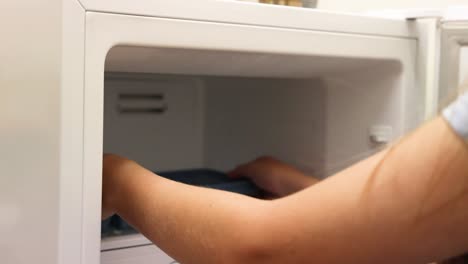 person filling and placing ice tray in freezer