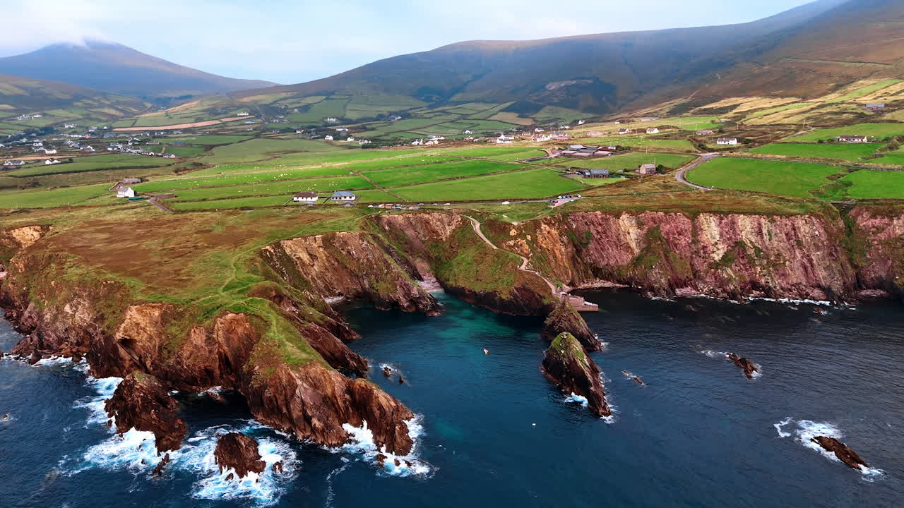 High cliff descending into the waters of the Atlantic Ocean. Approaching rocky shore of the Northern Ireland with a settlement in the valley. Top view.
