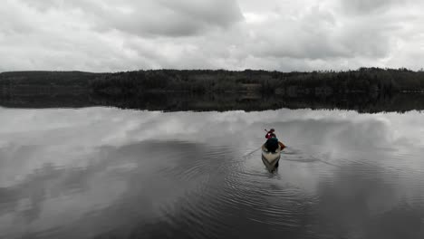 aerial - following people on a canoe on a lake, clouds reflecting on it, sweden